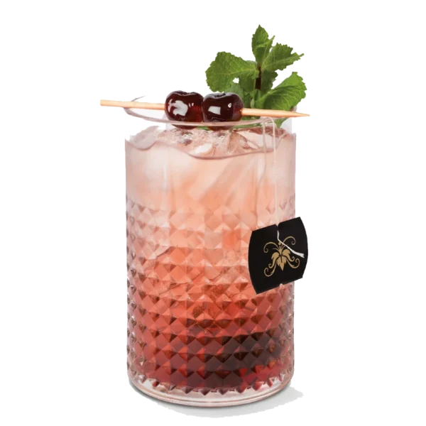 Drink gelado de coloração rosada servido com gelo, folhas de hortelã e cerejas como decoração em copo de vidro texturizado.