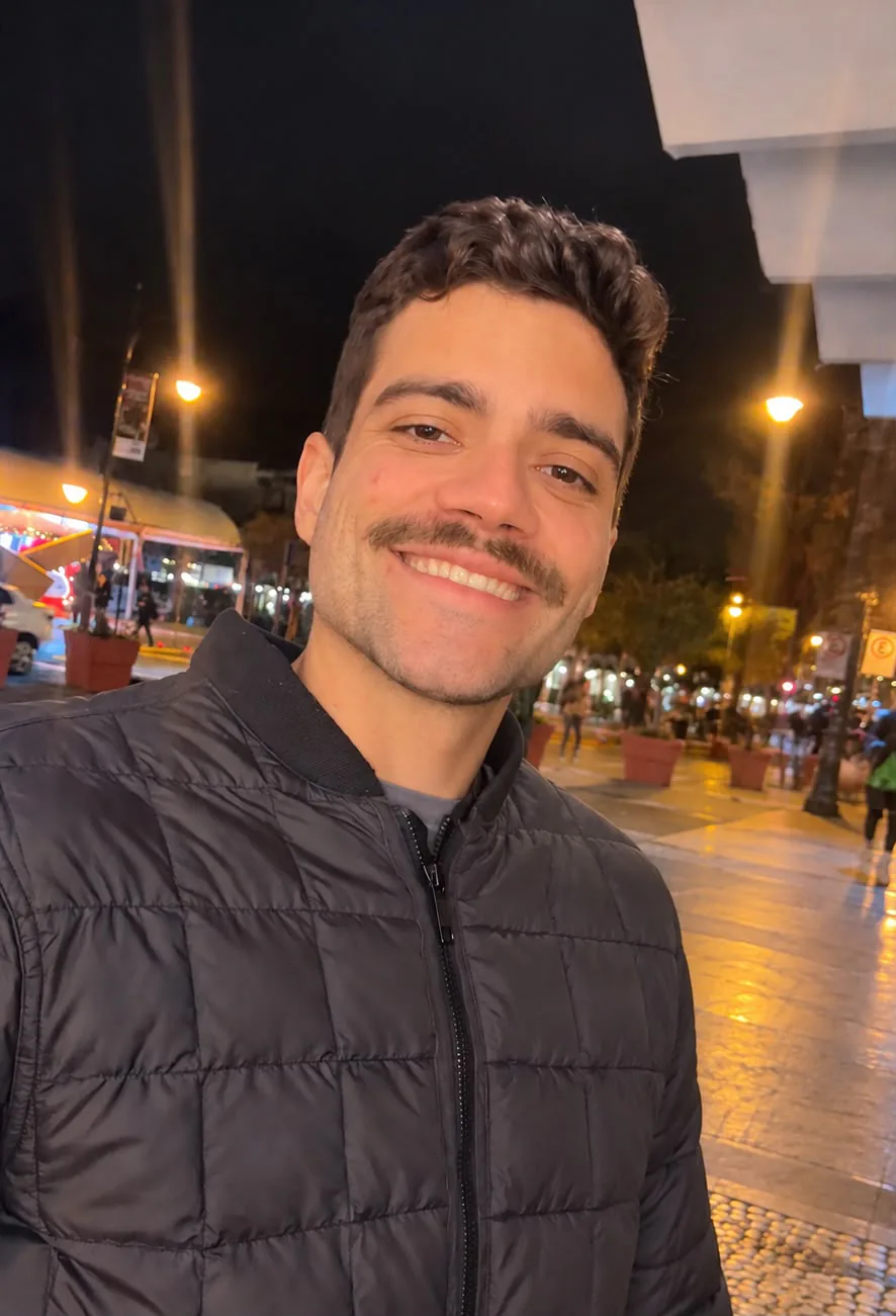 Retrato de Jorge Queiroz, gerente de vendas da GETU Shopping, sorrindo em uma rua iluminada à noite